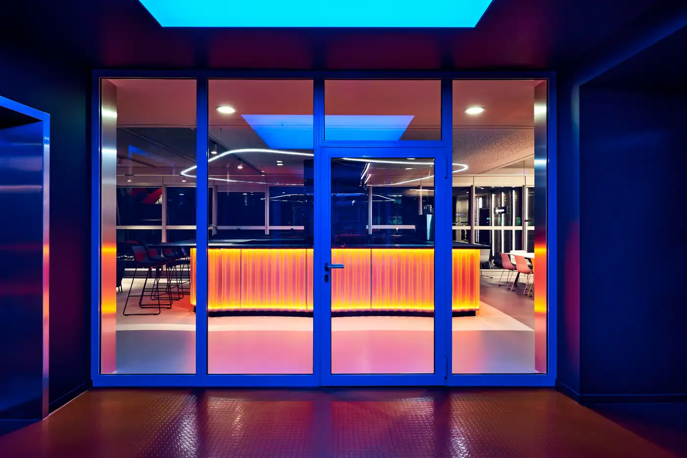 Glass entrance of everyworks at Berlin Hauptbahnhof at night, the glowing bar counter behind it