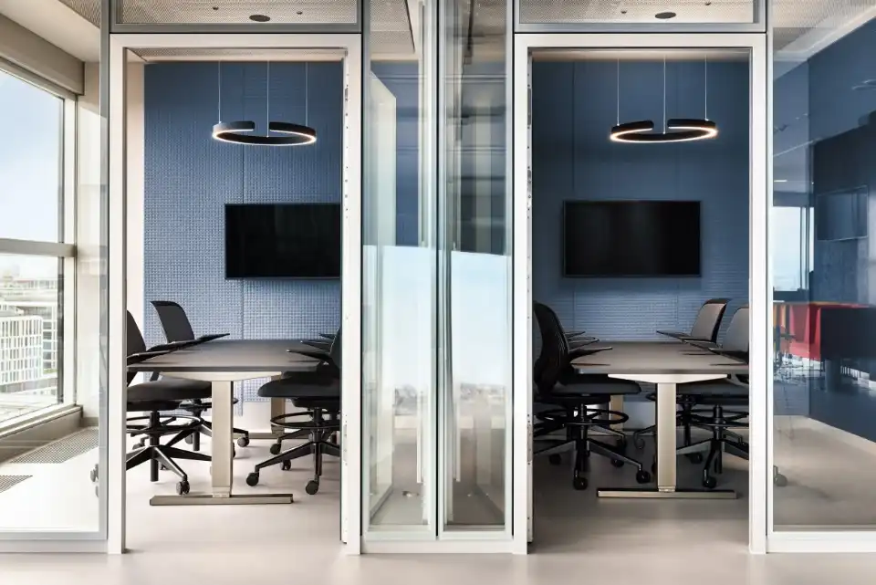 Glass meeting rooms with conference tables, screens and ring lights
